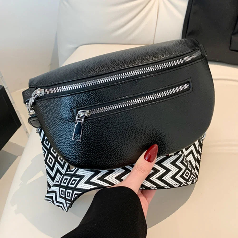A black PU leather multi-pocket crossbody bag with silver zippers is held by a hand against a white surface.