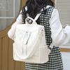 A woman is wearing a cream-colored leather anti-theft backpack over a plaid shirt.
