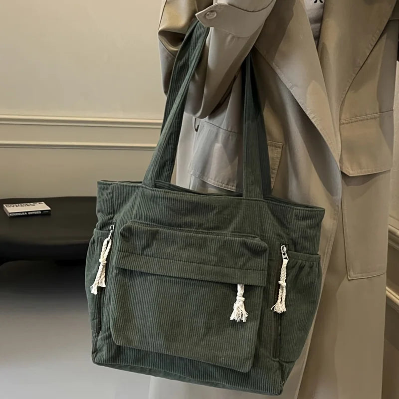 Un sac fourre-tout vert foncé en velours côtelé avec plusieurs poches est exposé sur un mannequin.