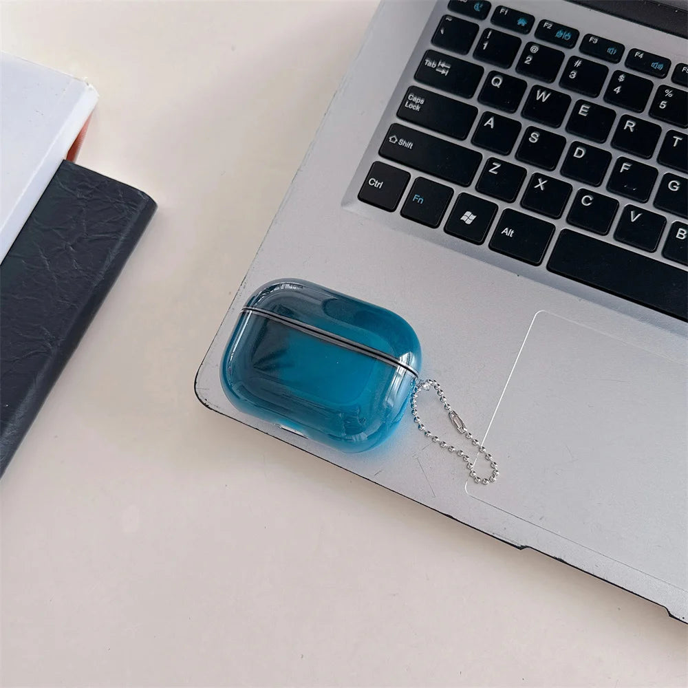 A small, translucent blue glass-like earphone case with a silver chain attached, resting on a silver laptop keyboard.