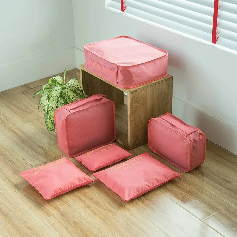 A set of pink mesh packing cubes stacked on a wooden shelf with a window in the background.