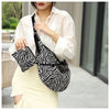 Eine Frau in weißem Hemd und hellem Rock hält eine schwarz-weiße Zebra-Canvas-Crossbodytasche.