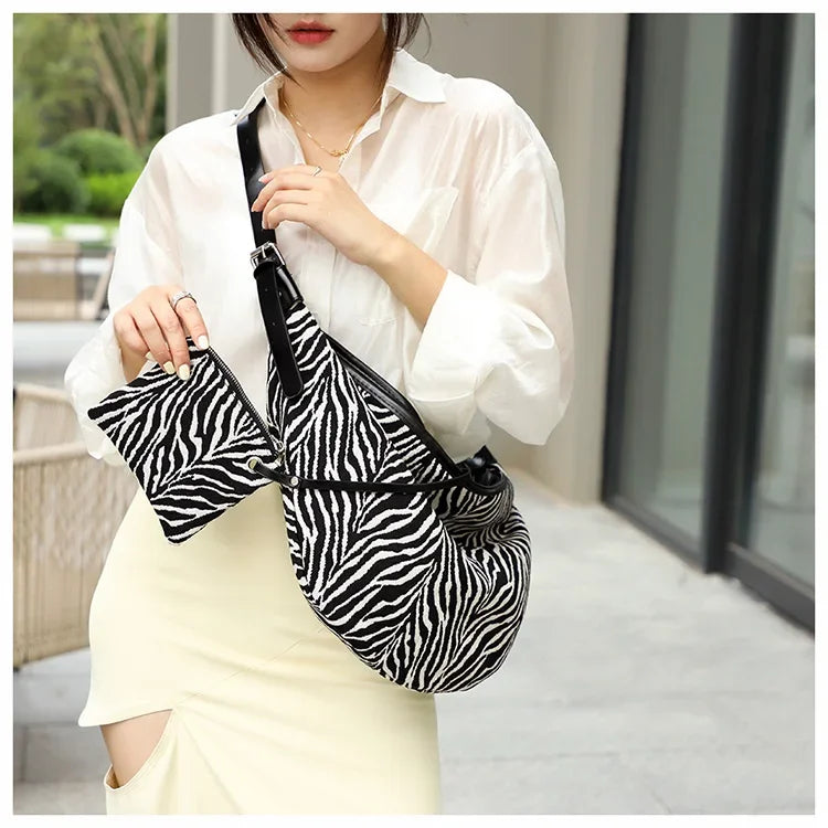 Eine Frau in weißem Hemd und hellem Rock hält eine schwarz-weiße Zebra-Canvas-Crossbodytasche.