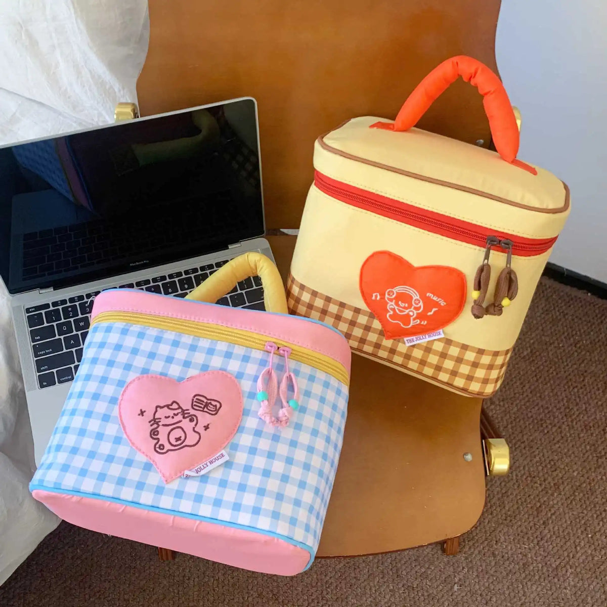 A yellow and red insulated lunch bag with a heart design and a pink checkered bag next to a laptop.