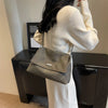 Una mujer sostiene un bolso de cuero gris en un suéter de punto blanco.