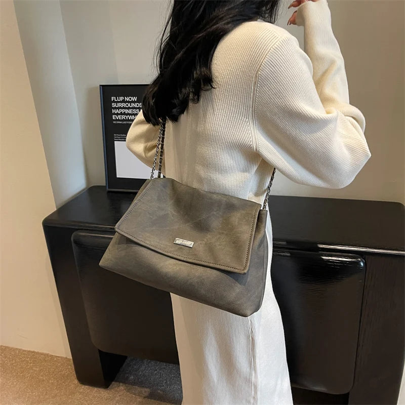 Una mujer sostiene un bolso de cuero gris en un suéter de punto blanco.