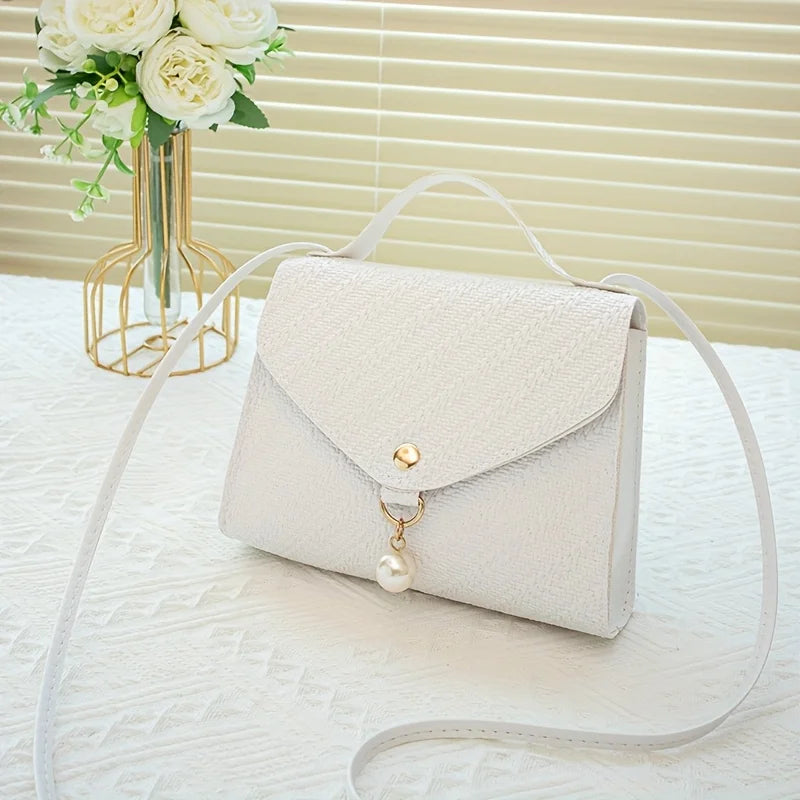 A cream-colored beaded square crossbody bag with a gold chain strap resting on a white surface.