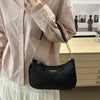 A black leather crescent crossbody bag with a gold chain strap is shown against a light pink blouse.