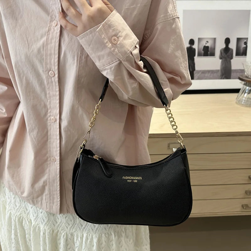 A black leather crescent crossbody bag with a gold chain strap is shown against a light pink blouse.