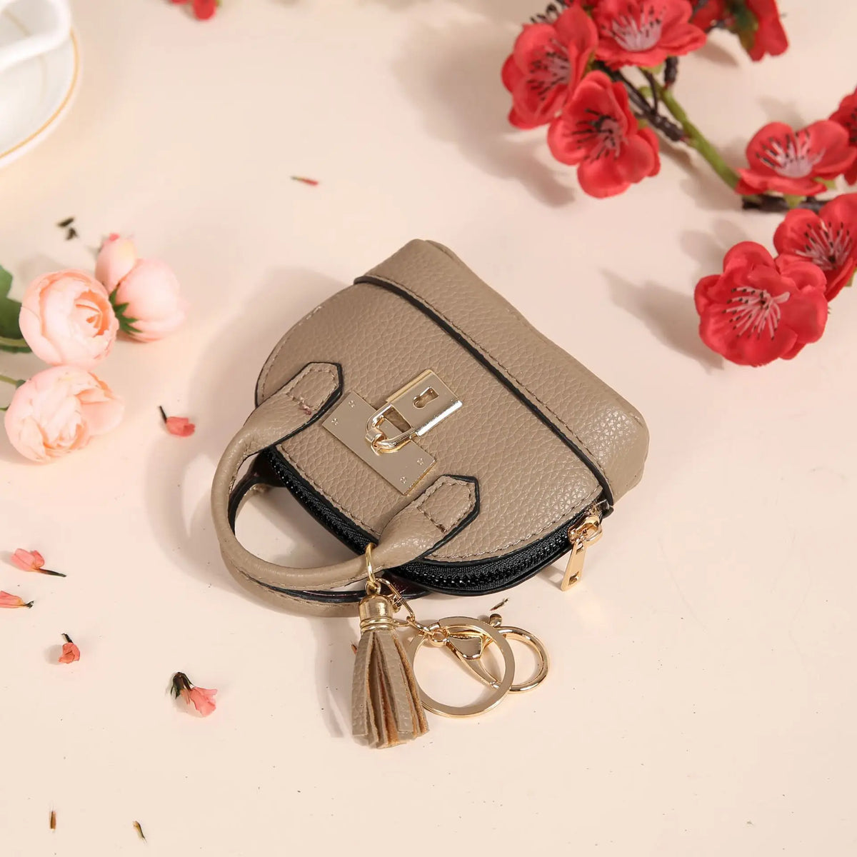 Portefeuille en PVC beige de luxe avec une clé en dorée, exposé sur un fond clair entouré de fleurs rouges.