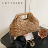 A close-up of a beige chain woven straw shoulder bag resting on a dark surface.