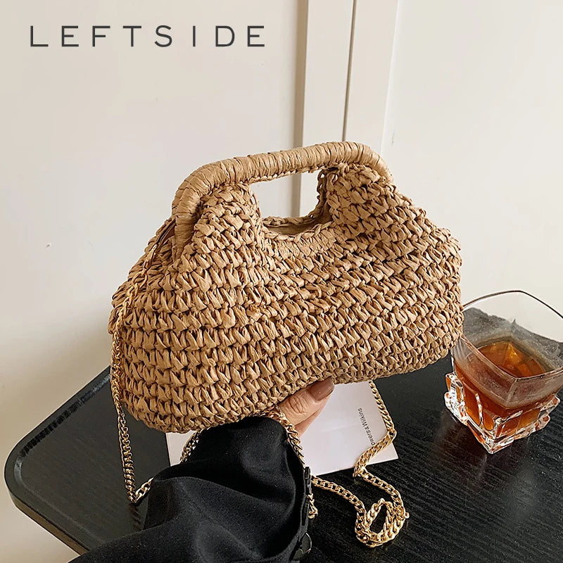A close-up of a beige chain woven straw shoulder bag resting on a dark surface.