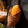 A plush keychain shaped like a roasted sweet potato with orange fluffy stuffing and a brown exterior.