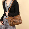 A woman wearing a black sweater and gray skirt holds a brown leather tote bag.