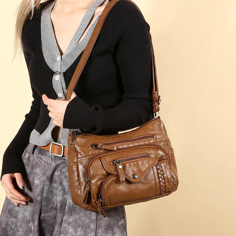 A woman wearing a black sweater and gray skirt holds a brown leather tote bag.