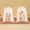 A set of six light beige drawstring gift bags featuring illustrations of Easter bunnies and carrots.