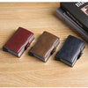 Three leather card holders in shades of burgundy, brown, and navy blue resting on a wooden surface.
