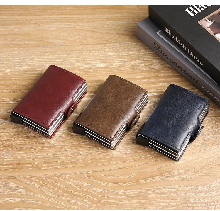 Three leather card holders in shades of burgundy, brown, and navy blue resting on a wooden surface.