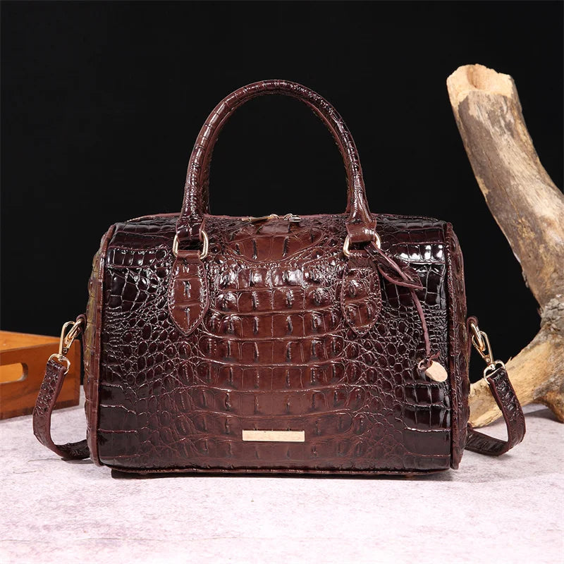 A dark brown crocodile pattern luxury leather crossbody tote bag with a handle resting on a light surface.