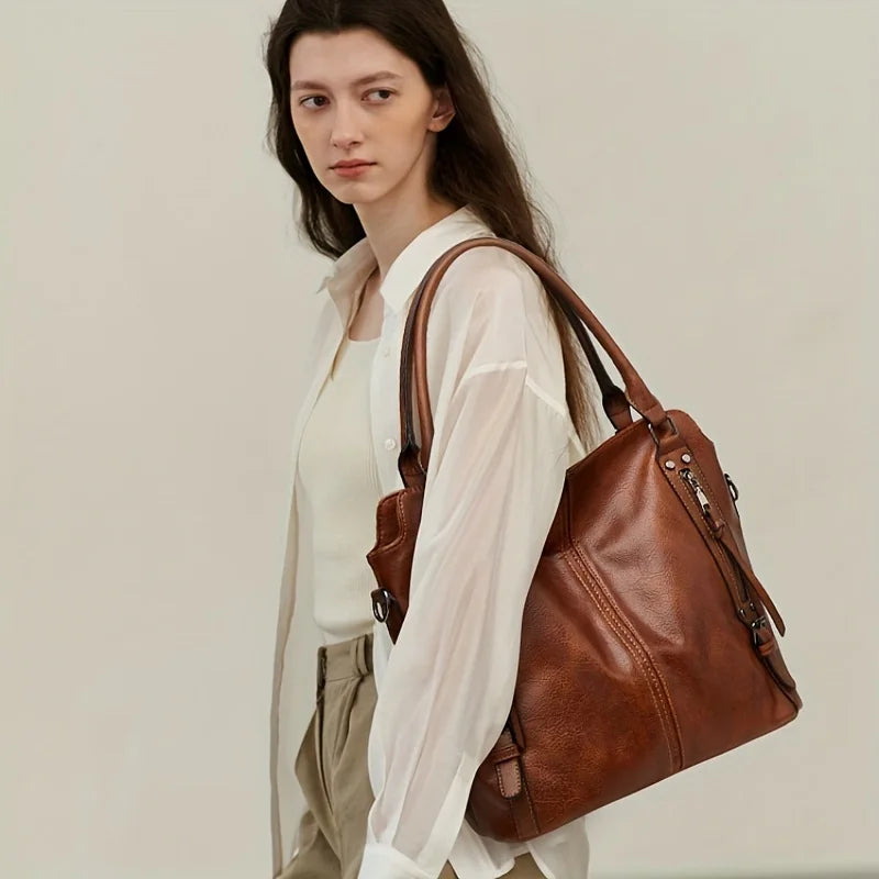 A woman models a brown PU leather crossbody tote bag with sheer white blouse and light trousers.