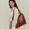A woman models a brown PU leather crossbody tote bag with sheer white blouse and light trousers.