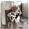 A hand holds a leopard print faux leather wrist bag against a light sweater and tan fabric.