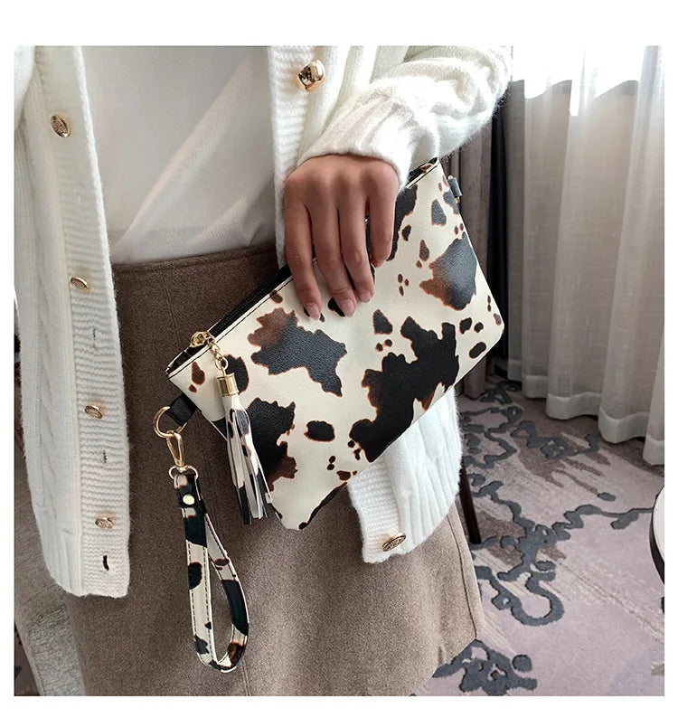 A hand holds a leopard print faux leather wrist bag against a light sweater and tan fabric.