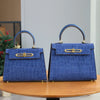 A deep blue leather tote bag with a crocodile pattern and gold hardware displayed on a wooden table.