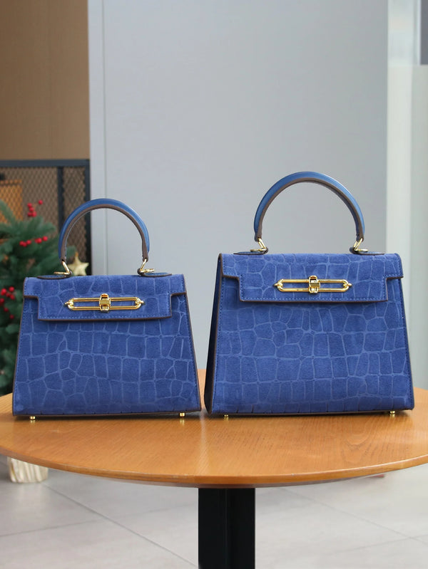 A deep blue leather tote bag with a crocodile pattern and gold hardware displayed on a wooden table.