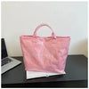 A pink satin tote bag is displayed on a dark surface next to a laptop and some papers.