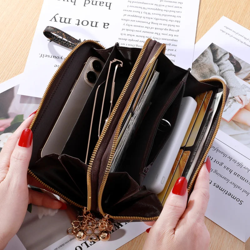 Cartera con cremallera de cuero falso marrón y detalles dorados abierta, mostrando tarjetas y una tarjeta de crédito.