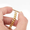 A hand holds a delicate gold chain strap with a rectangular clasp, showing its texture and shine.