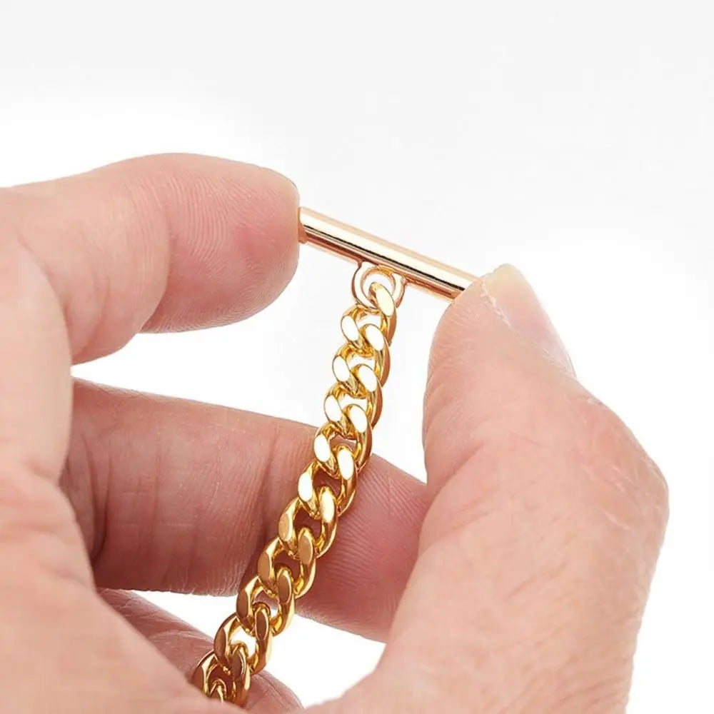 A hand holds a delicate gold chain strap with a rectangular clasp, showing its texture and shine.