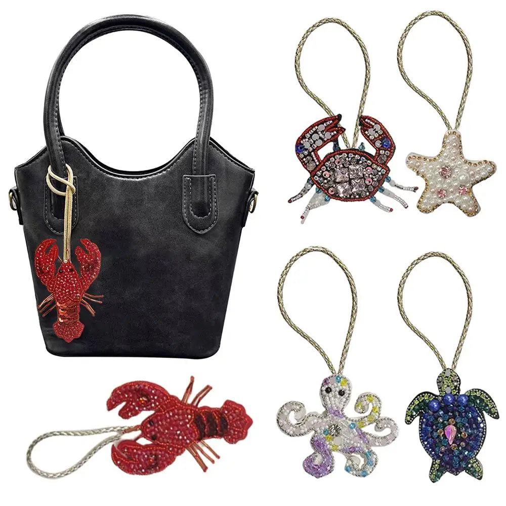 A black leather bag charm featuring a red crab and a starfish, along with several other rhinestone beaded charms.