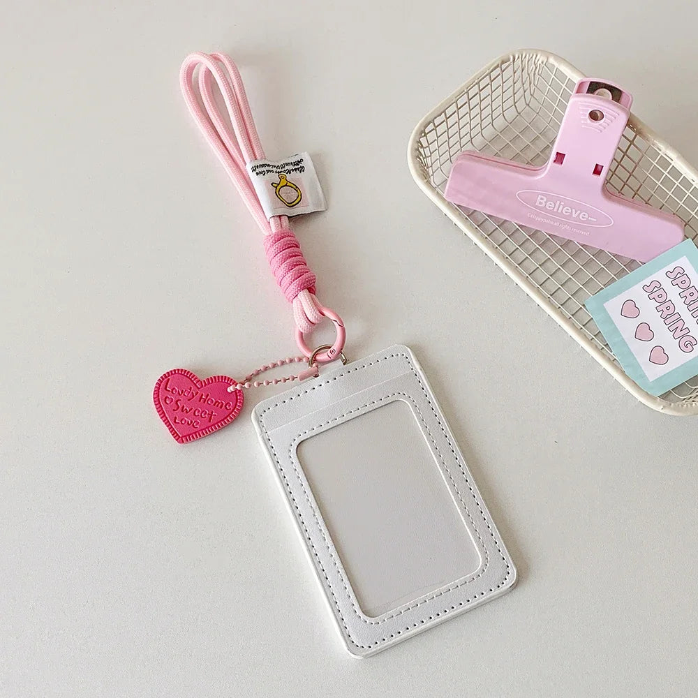 A pink PU credit card and ID holder keychain with a heart charm and a matching pink lanyard resting on a white background.