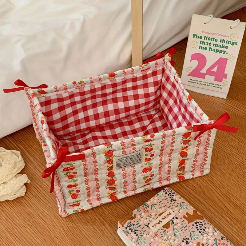 A quilted cotton storage basket with a red and white checkered pattern and lace flower design sits on a wooden surface.