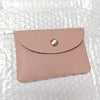 A pale pink genuine leather card holder with a gold-toned stud closure.