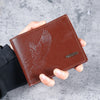 A brown leather wallet with an embossed eagle design is held in a person's hand against a gray background.