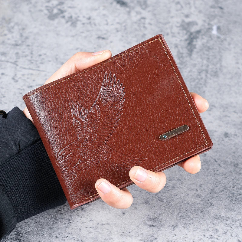 A brown leather wallet with an embossed eagle design is held in a person's hand against a gray background.