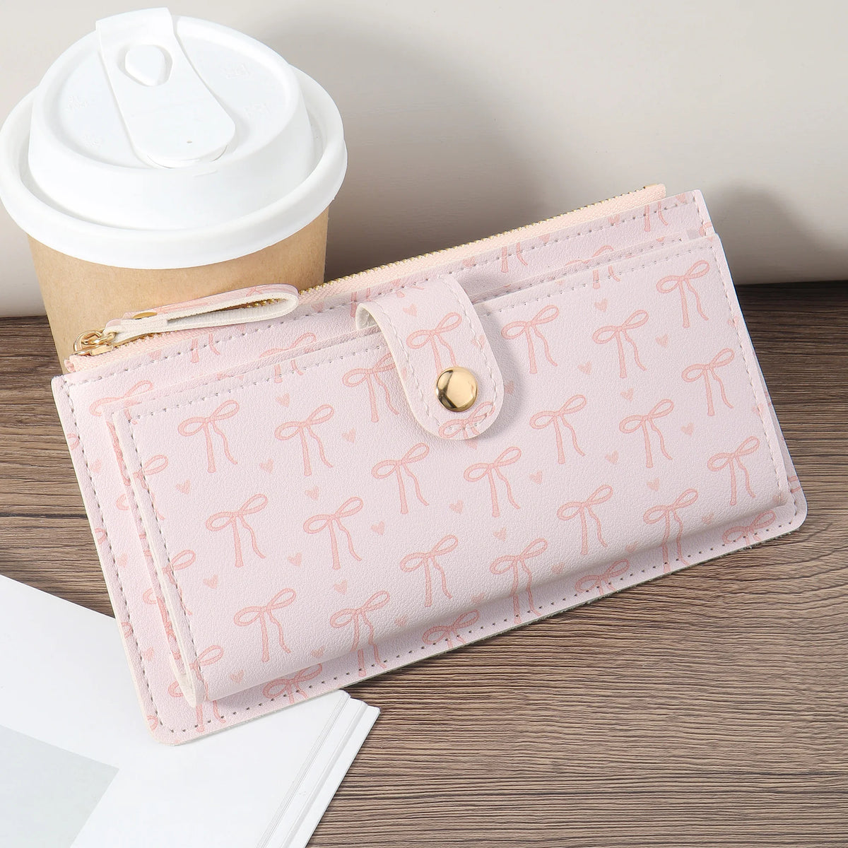 A pink folding multi-card wallet with a decorative bow detail is shown next to a paper cup.