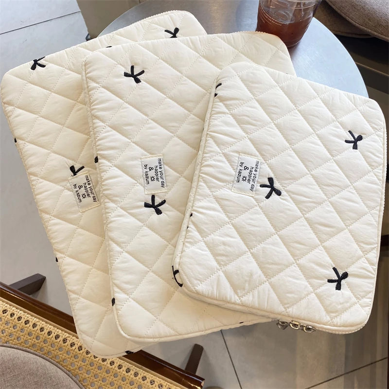 A stack of cream quilted laptop sleeves for MacBook and tablet