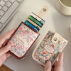 A hand holds a floral patterned leather card wallet next to a stack of credit cards on a white desk.
