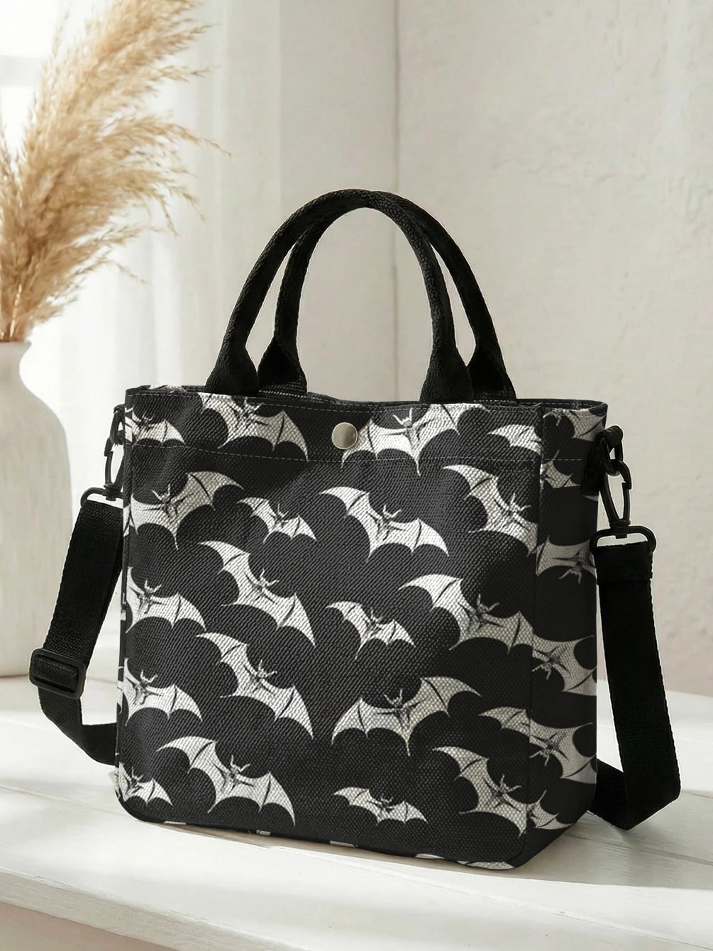 Black tote bag with a white bat print and black strap resting on a white surface.