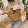 A person wearing a white shirt holds a handwoven straw moon bag with a top handle.
