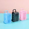 Three miniature doll suitcases in blue, black, and pink plastic are displayed on a light blue surface.