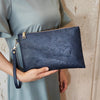 Una mano sostiene un bolso de cuero sintético azul oscuro con estampado floral contra un vestido verde claro.