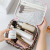 A hand opens a leopard print travel makeup organizer bag revealing various skincare and cosmetic products.