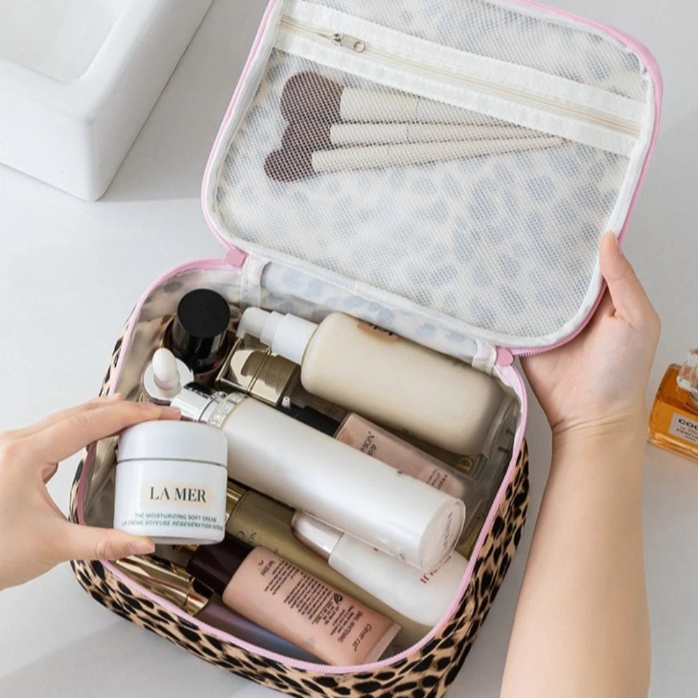 A hand opens a leopard print travel makeup organizer bag revealing various skincare and cosmetic products.