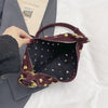 A dark burgundy faux suede hobo crossbody bag with gold rivet accents resting on a gray folder.