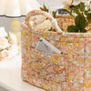 A quilted fabric storage basket with light floral pattern and carry handles sits on a white surface.